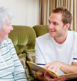 Young male carer reading to elderly woman