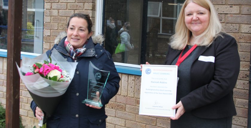 Two women at award presentation with flowers and certificate