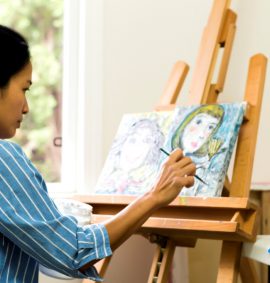 Woman in blue striped shirt painting a picture on an easel