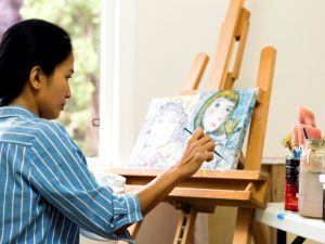 Woman in blue striped shirt painting a picture on an easel