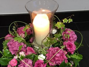 Pink and green flower arrangement with glass vase and candle in the middle