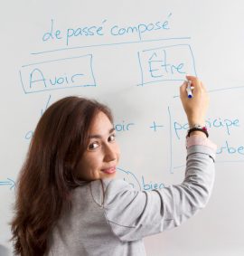 Woman writing on French verbs on whiteboard