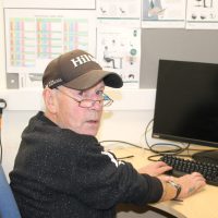 man sitting at desk in cap and glasses with computer