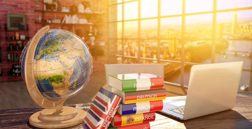 A globe, a pile of language books and a laptop on a desk