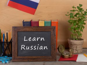 Blackboard with Learn Russian written with pencils and books behind