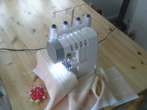 Overlocker sewing machine on wooden table with cloth and pincushion
