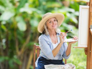 Woman in a hat painting on an easel outside