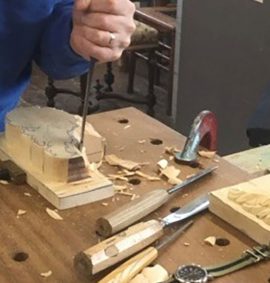 Man in blue sweater wood carving with chisel