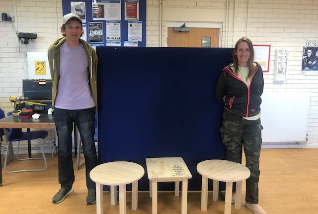 A man and a woman with three wooden tables that they made