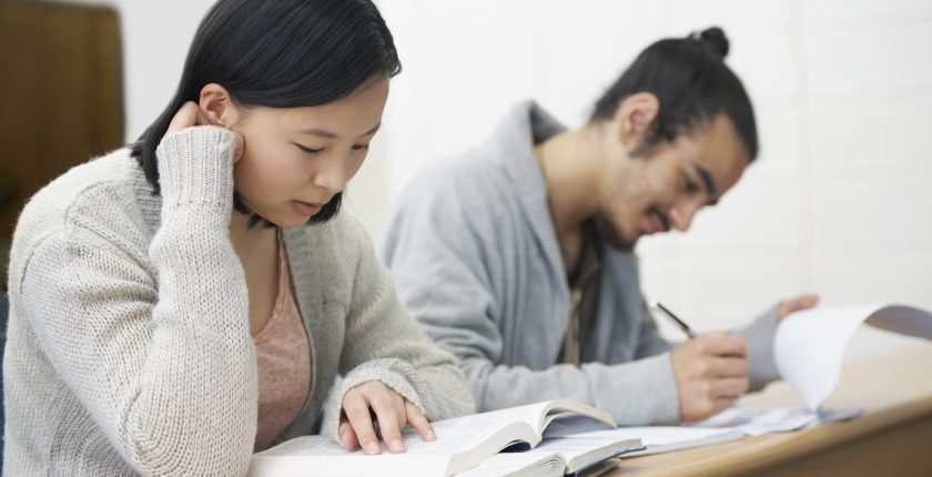 Image of two students sitting in a lecture hall and studying for exams