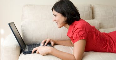 Woman using laptop lying on a sofa