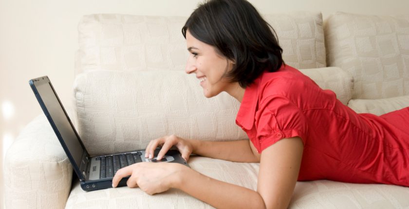 Woman using laptop lying on a sofa